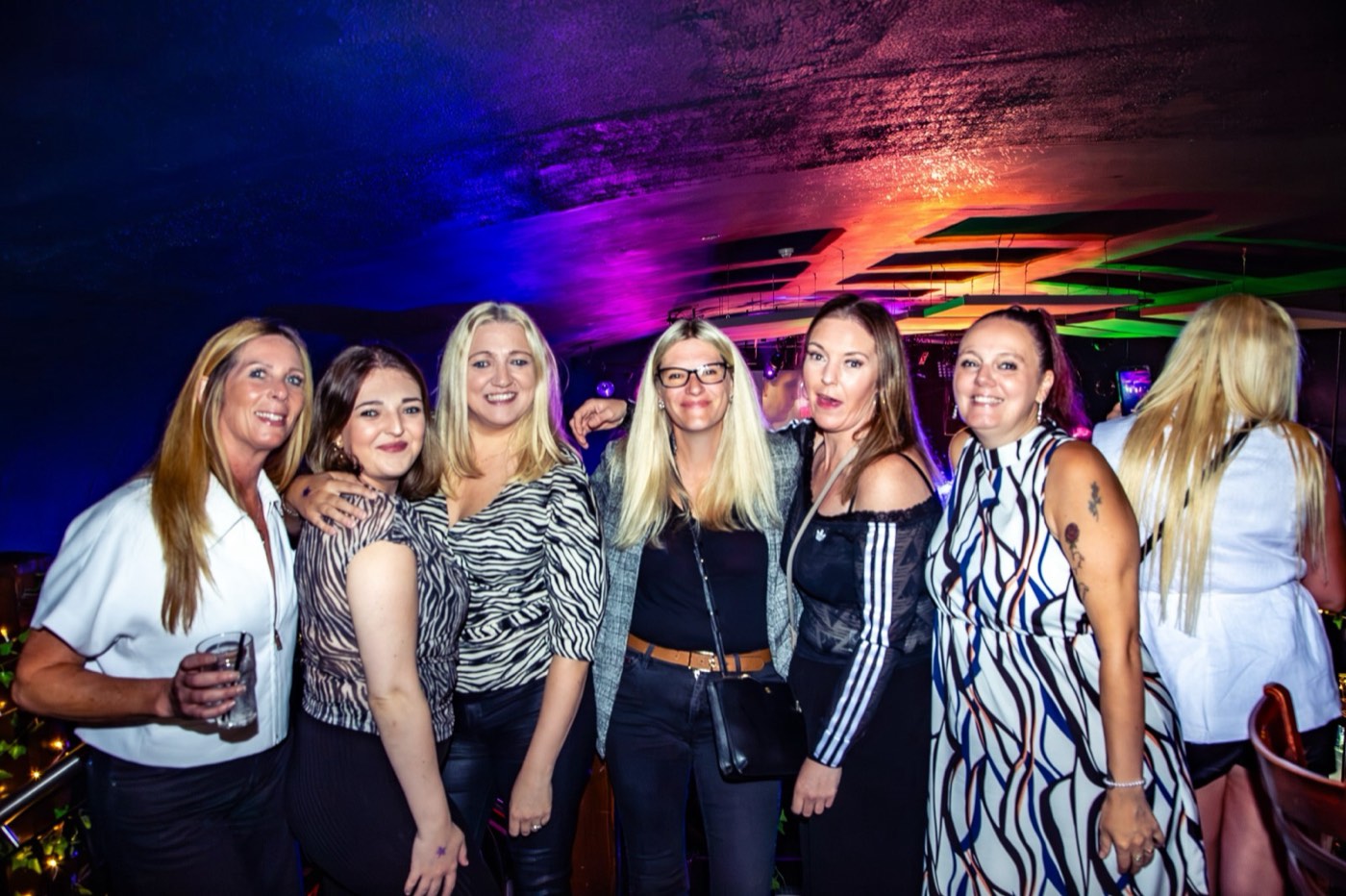 A group of friends posing under rainbow lights