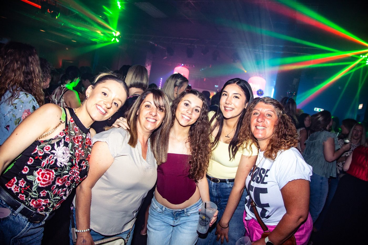Five friends smiling together under green lasers