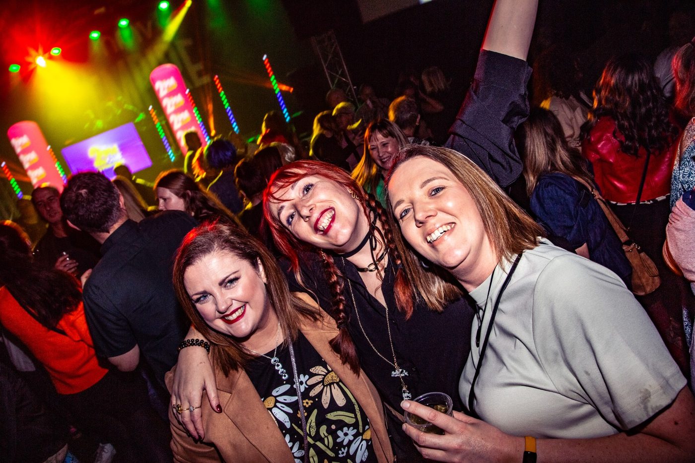 Three friends laughing together with stage lights behind