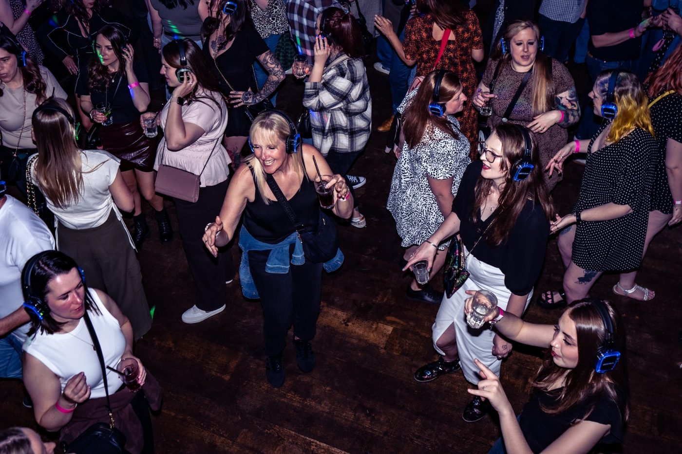 Friends dancing with drinks in light-up headphones