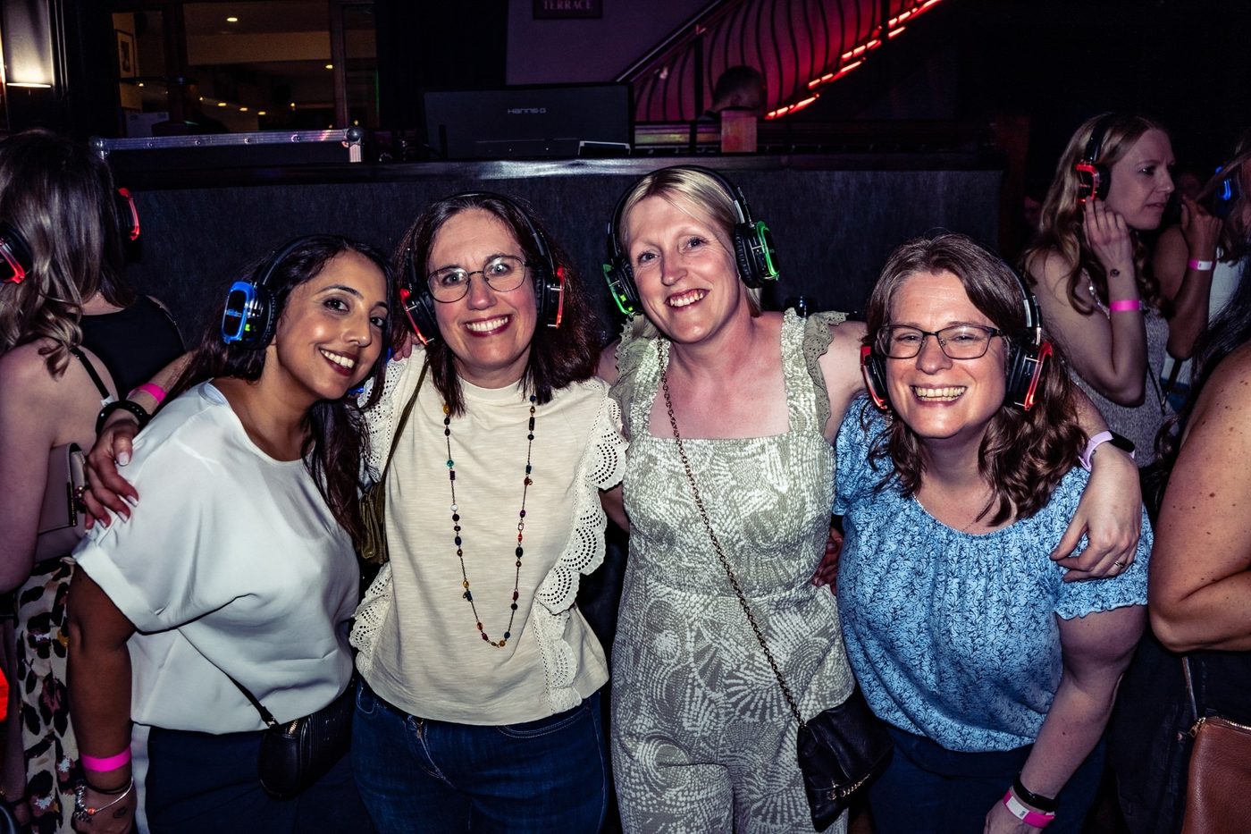 Four friends smiling together in light-up headphones